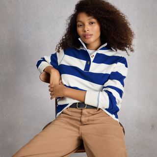 Woman wearing a blue and white striped shirt with beige pants against a gray background