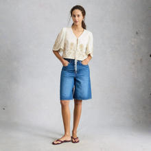 Load image into Gallery viewer, Woman wearing a white embroidered top and blue denim shorts against a gray background
