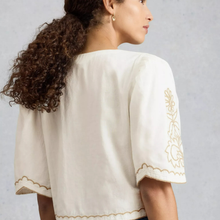 Load image into Gallery viewer, Woman wearing a white blouse with gold embroidery on a gray background
