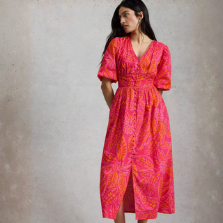 Woman wearing a pink and orange patterned dress against a plain background