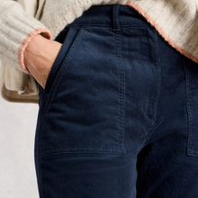 Load image into Gallery viewer, Close-up of a person wearing dark navy corduroy pants with a hand in the pocket, paired with a cream knit sweater with pink fringed trim.
