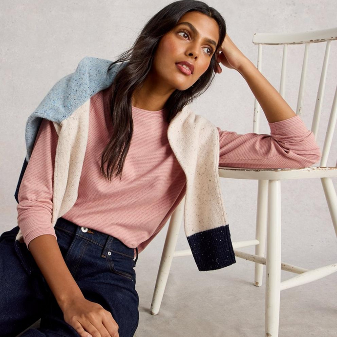 Woman sitting on a chair wearing a pink sweater and patterned cardigan.