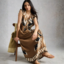 Load image into Gallery viewer, Woman sitting on a chair wearing a patterned dress against a gray background
