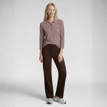 Load image into Gallery viewer, A woman modeling a long-sleeve collared polo shirt with thin red and white horizontal stripes, paired with dark brown pants and gray sneakers, against a light gray studio background.
