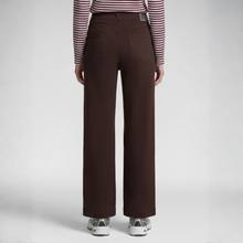 Load image into Gallery viewer, A person shown from the back wearing dark brown wide-leg trousers, a red and white striped long-sleeve top, and white sneakers against a light gray studio background.
