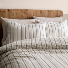 Load image into Gallery viewer, Striped bedding with pillows on a bed with a wooden headboard.
