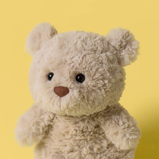 Closeup of Jellycat Bartholomew Bear Junior, with yellow background.