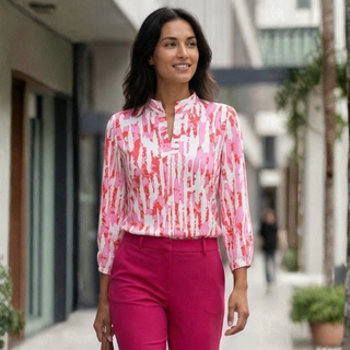 Woman wearing a pink and white patterned blouse with pink pants walking outdoors.