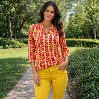 Woman wearing a colorful patterned blouse and yellow pants standing in a garden.