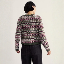 Load image into Gallery viewer, A person shown from the back wearing a long-sleeve knit sweater with a multicolor geometric Fair Isle pattern in pink, green, and gray, paired with dark charcoal pants against a plain off-white background.
